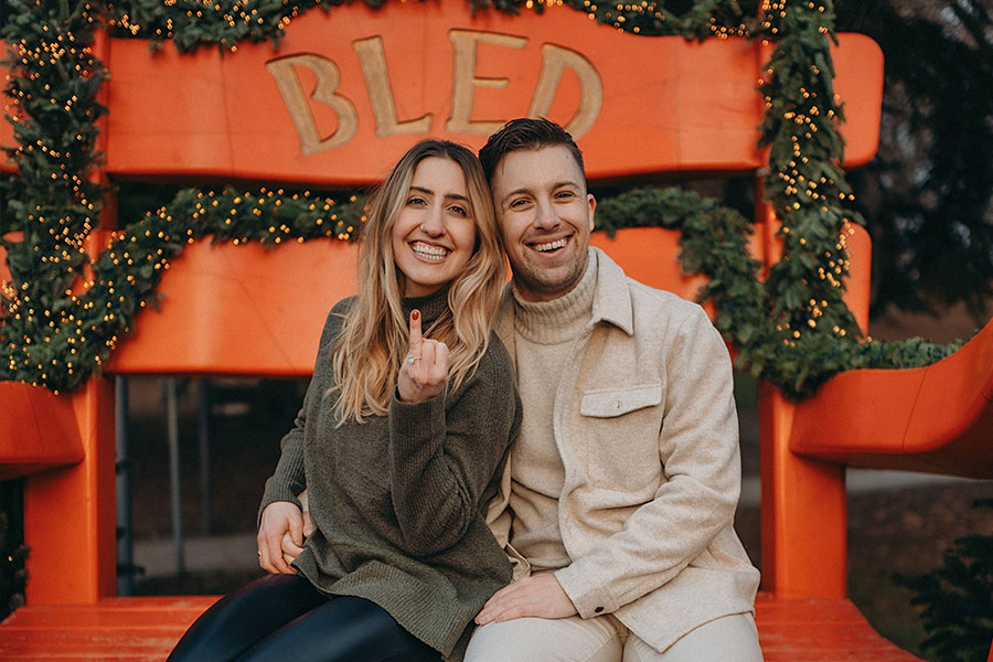 Newly engaged couple smiling at the Bled sign and showing the engagement ring