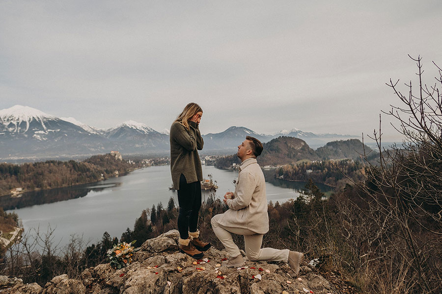Lake Bled proposal on one knee at a mountain viewpoint with the lake and Alps behind