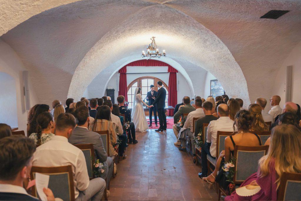 Intimate wedding ceremony inside the Knights' Hall at Bled Castle with seated guests, organised by Petra Starbek.