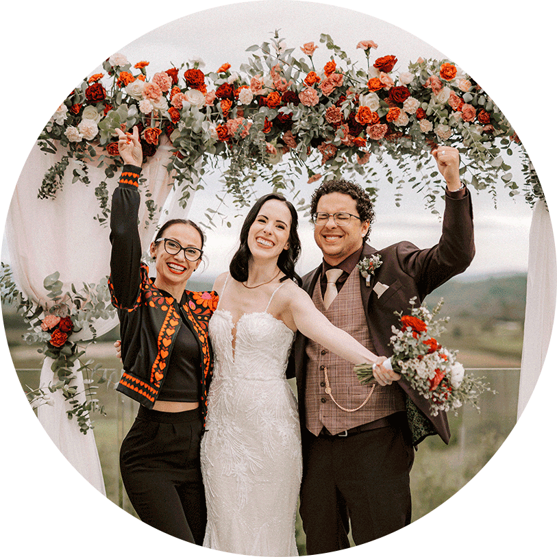 Wedding planner Petra Starbe and happy couple under an arch with red, white, soft pink flowers for boho wedding in Slovenian Tuscany.