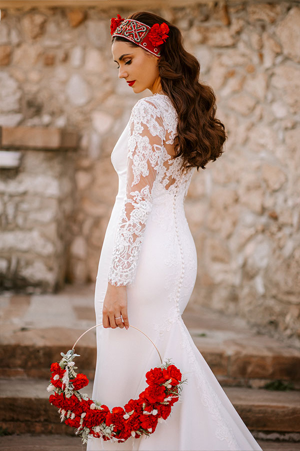 A close photo of a bride with perfect makeup and hair in a white wedding dress, red circle bridal bouquet, and red flowers in her hair.