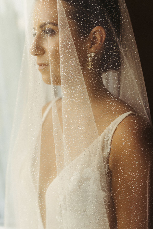 Close up photo of a Bride with Chanell earrings, shinny veil and white wedding dress with a V-neckline.