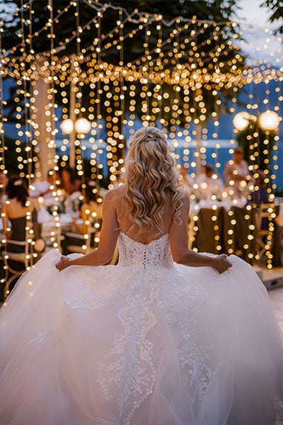Back view of a Bride in her princess wedding dress walks to her wedding table under fairy lights tunnel at Grand hotel Toplice, Lake Bled at night.