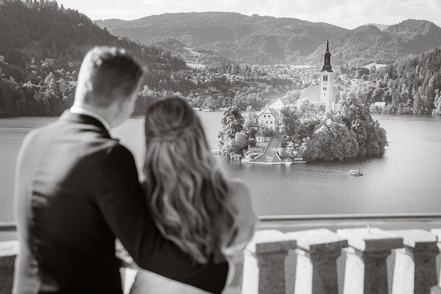 Black and white photo of a wedding couple who looks at lake Bled island church.