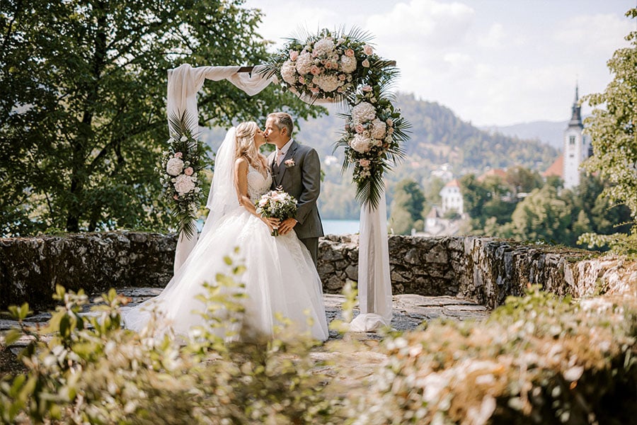 An amazing newlyweds are kissing in front of a wooden arch with flowers and linen after their wedding ceremony at vila Bled,