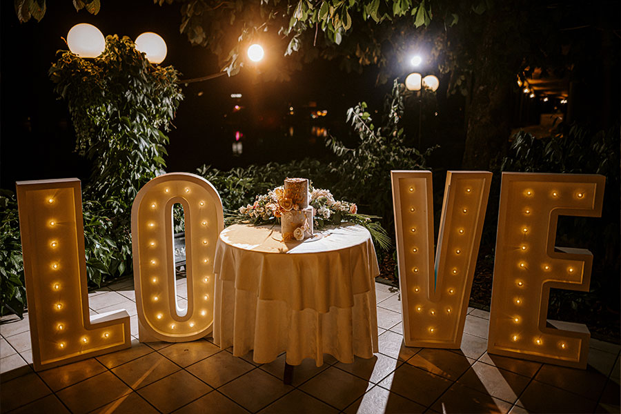 A gorgeous pastel wedding cake with gold unique sign stands in the middle of love sign on Grand hotel Toplice terrace.