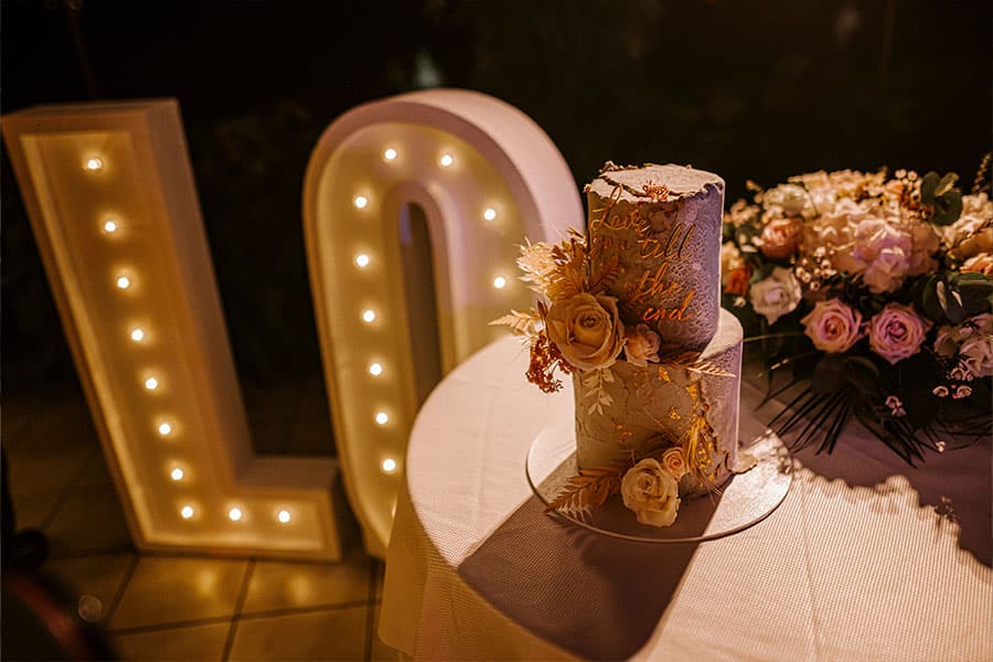 Closer view of a gorgeous pastel wedding cake with gold unique sign and fresh roses stands in the middle of love sign on Grand hotel Toplice terrace.