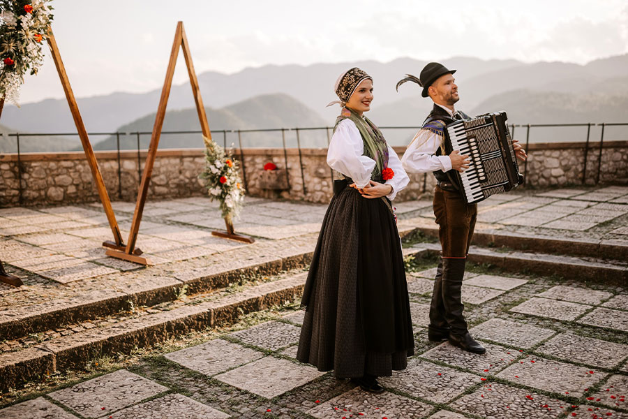 A lady and a gentleman with a harmonica in a traditional folklore dancers suits at lake Bled Castle reception.