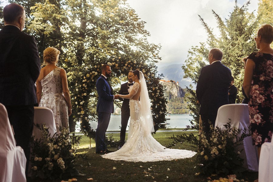 Bride in a Galia Lahav wedding dress and groom are standing in front of circle flower arch at their wedding ceremony at Vila Bled.