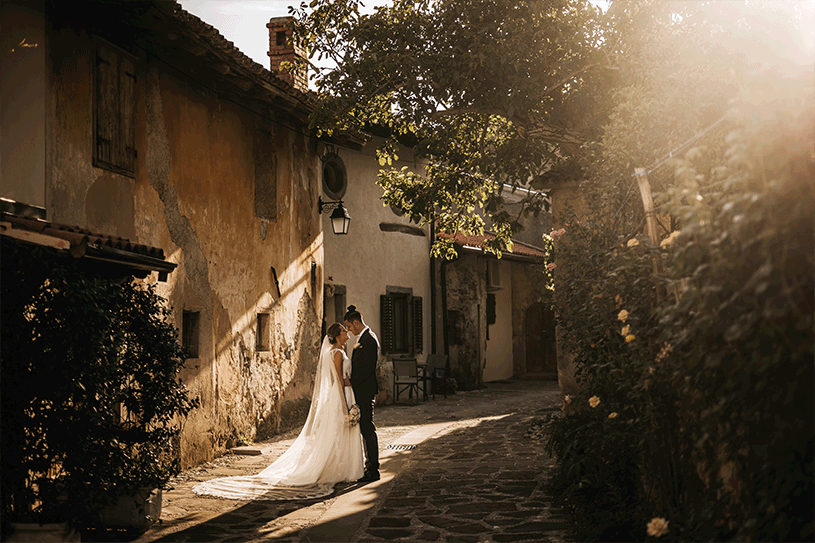 Newlywed young affectionate and amorous in wedding dresses standing in front of one another and holding hands on their wedding day in Slovenia.
