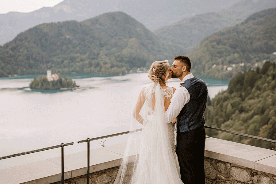 Couple stand by the Lake Bled castle fence during their Lake Bled elopement and kissing.