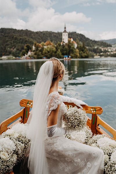Bride on a decorated boat with white flowers goes to Lake Bled Island.