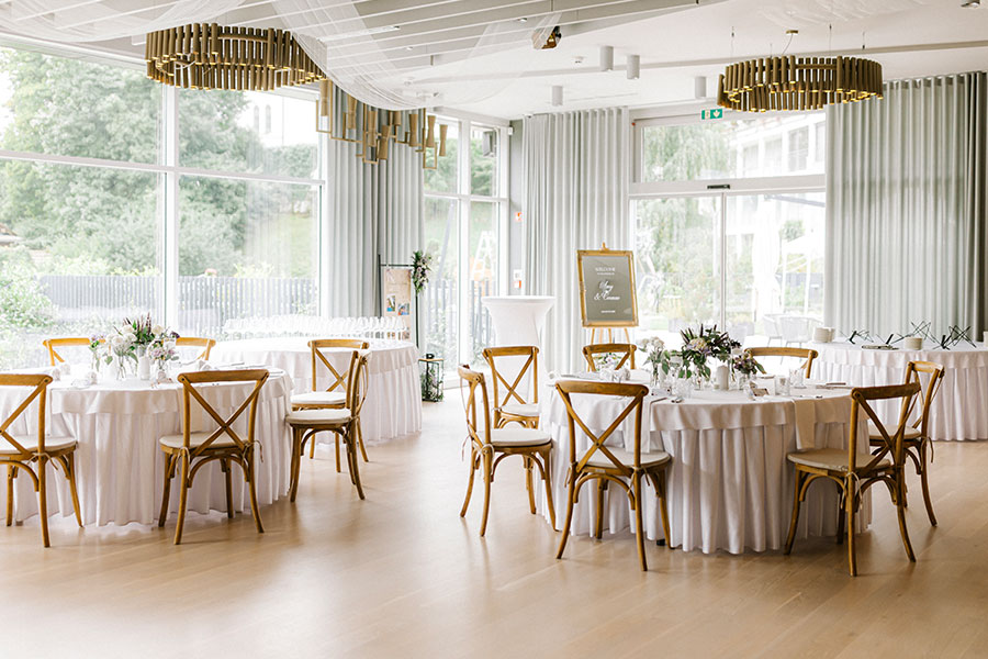 Elegant indoor wedding reception setup at a luxury Lake Bled hotel with round tables, natural light, and refined décor.