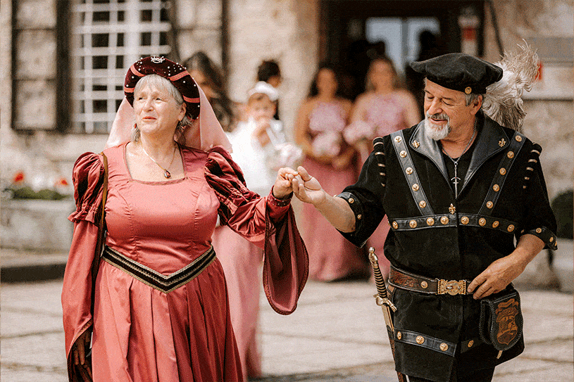 Couple in medieval dresses holding hands leads wedding guest to the wedding ceremony place at Lake Bled Castle.