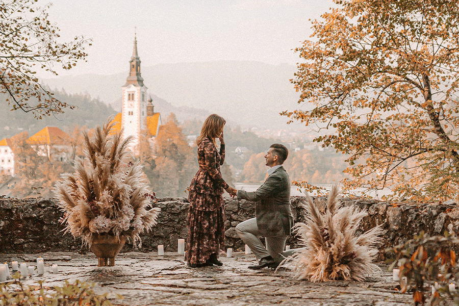 Surprise engagement at Lake Bled. Guy standing on his knee and offering engagement ring to his girlfriend on vila Bled terrace which was nicely decorated with flowers, candles and autumn leaves..