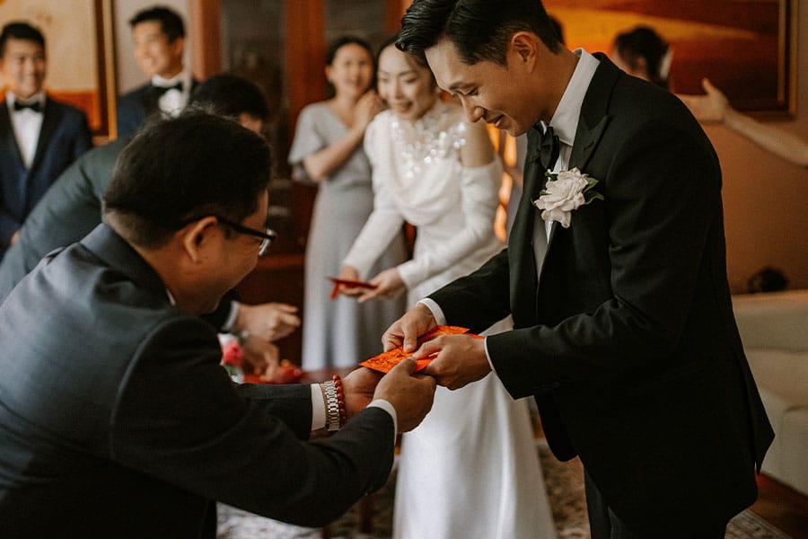 This image is a beautiful snapshot of a Chinese tea wedding ceremony, encapsulating the joy, love, and formal elegance of the occasion. Parents give the bride and the groom red envelopes in Vila Bled, Lake Bled.