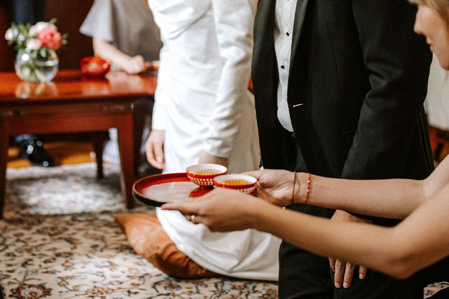 A person holding a tray of small cups in front of a groom and a bride during a Chinese tea ceremony in Vila bled, lake Bled.