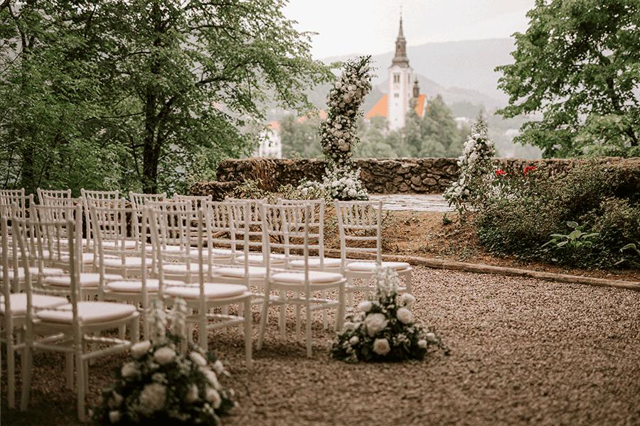 The luxury ceremony setting is in green-white colors. White chairs with flower decorations next to them for guests and two side flower arches were the perfect choices for destination wedding couples from Korea.