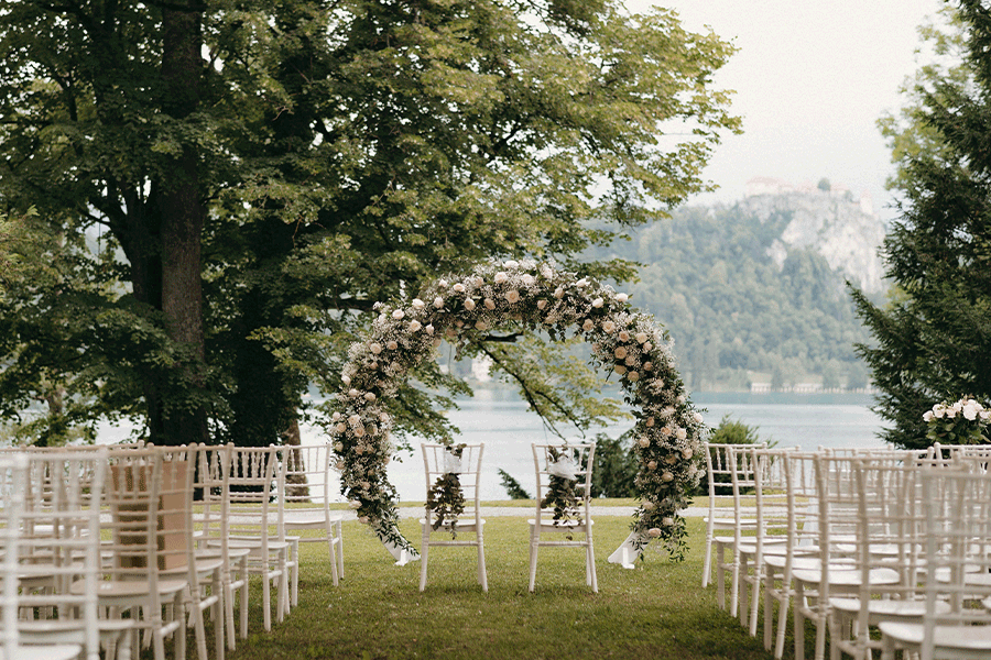 Intimate setting for a small wedding ceremony at vila Bled park with a flower circle arch and white chairs.