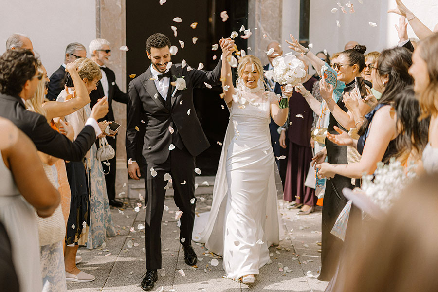 Newlyweds walking out after the ceremony with confetti and guests cheering at a Lake Bled wedding.