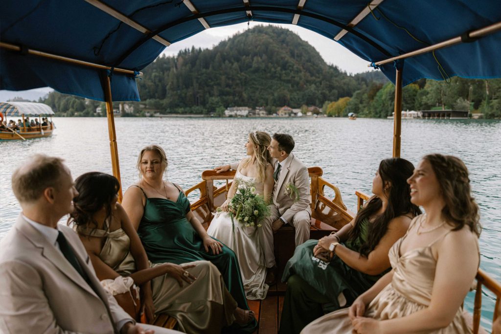 Bride, groom and wedding guests travelling on a traditional pletna boat across Lake Bled, wedding planned by Petra Starbek.