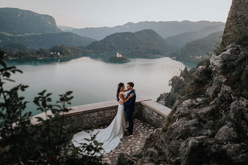 Bride and groom are hugging at lower Lake Bled Castle terrace with a view on Lake Bled.