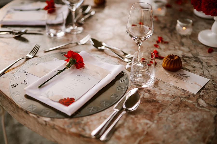 An elegant and luxurious wedding set up for dinner at Bled Castle - wedding name card, wedding menu, thank you note, red carnation on napkin, glasses, cutlery...