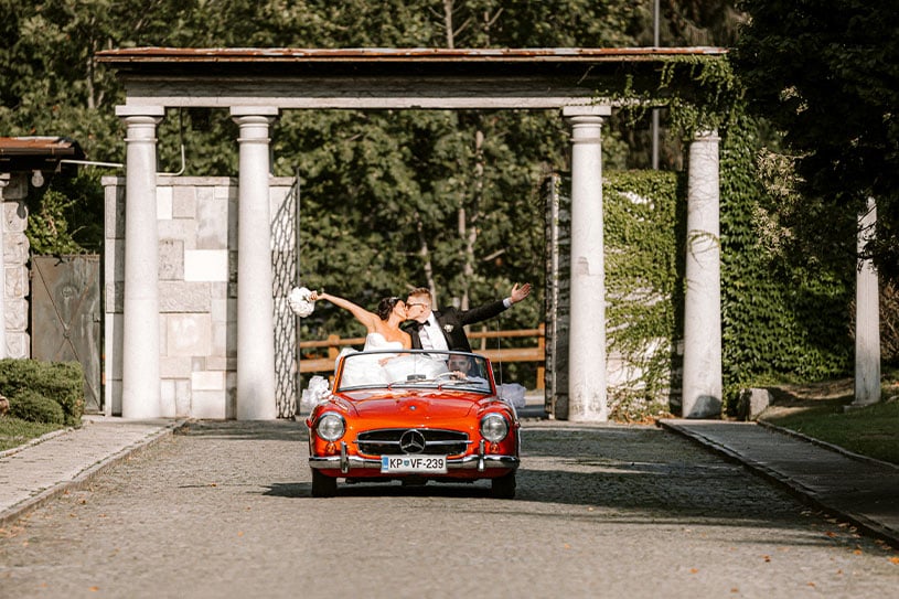 Wedding couple kissing in a red cabrio which drives to the villa Bled.