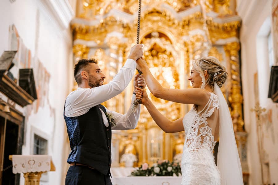 Happy and relaxed wedding couple is ringing a wishing bell in Lake Bled Island Church.