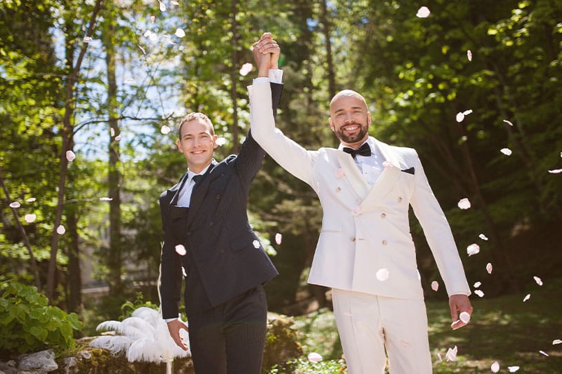 Smiling newlywed same-sex couple holding hands hing in the air after their wedding ceremony at Lake Bled in Slovenia.