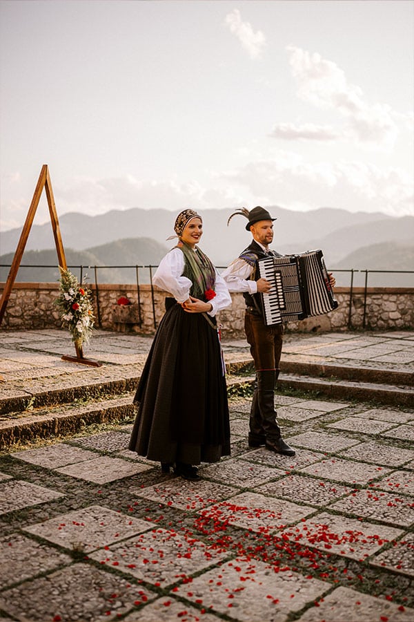 Boy in folk dress plays accordion and a girl in a folk dress at lake Bled Castle.