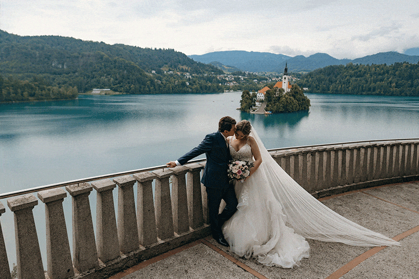 A wedding couple from France embraces during a wedding photo shoot on the bridge of Villa Bled with a view of Bled Island.