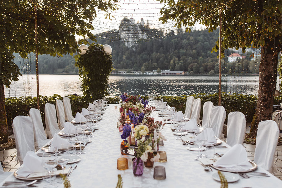 A beautiful summer-decorated wedding table at the Lake Bled shore for an intimate wedding dinner and upper the table are twinkle lights.