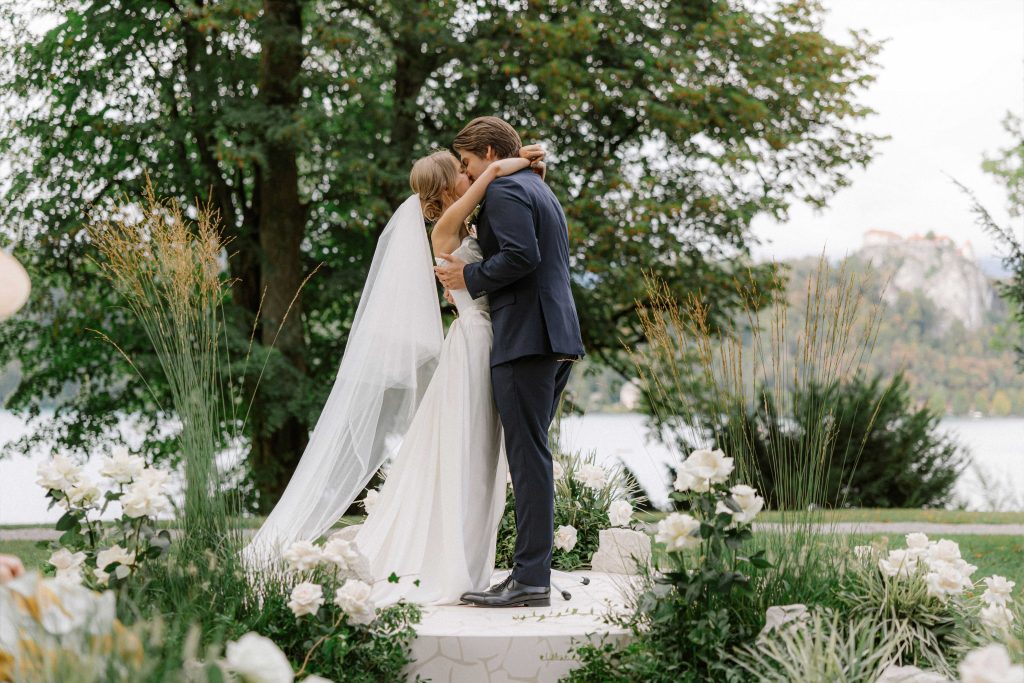 Bride and groom sharing a kiss during their intimate wedding ceremony in the gardens of Vila Bled, overlooking Lake Bled, planned by Petra Starbek.