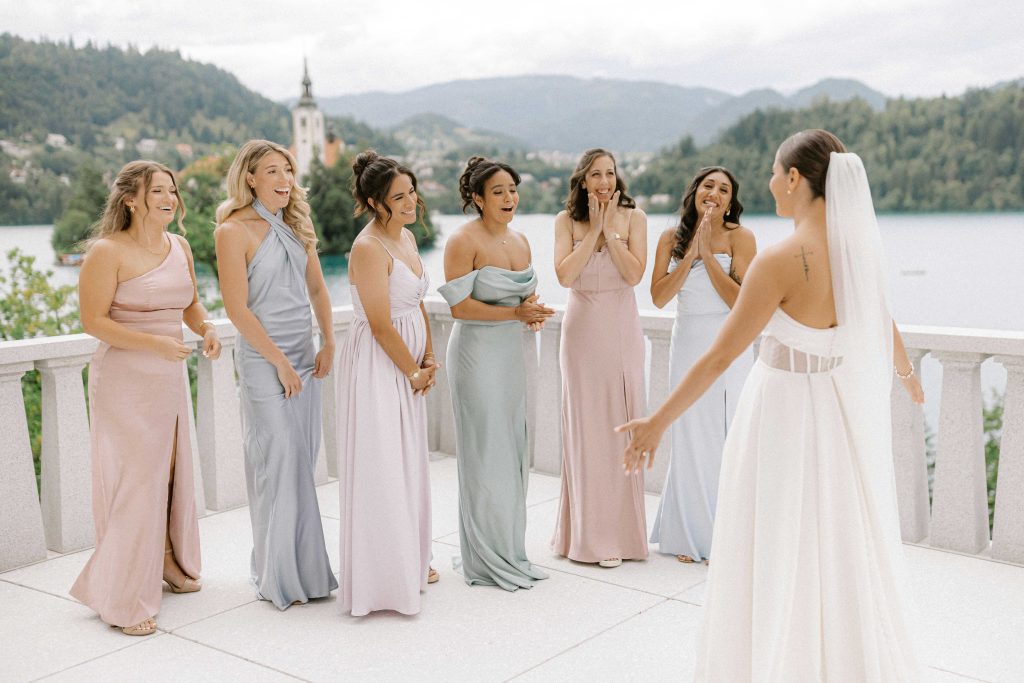 Bride sharing a first-look moment with her bridesmaids on the terrace overlooking Lake Bled, wedding by Petra Starbek.