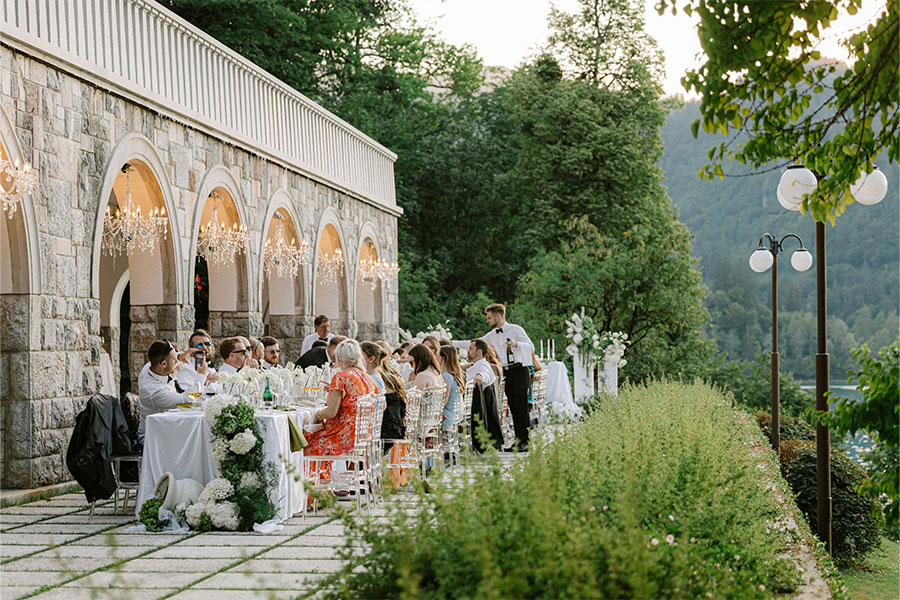Wedding guests dining together at a long outdoor table beneath chandeliers on the Vila Bled terrace.