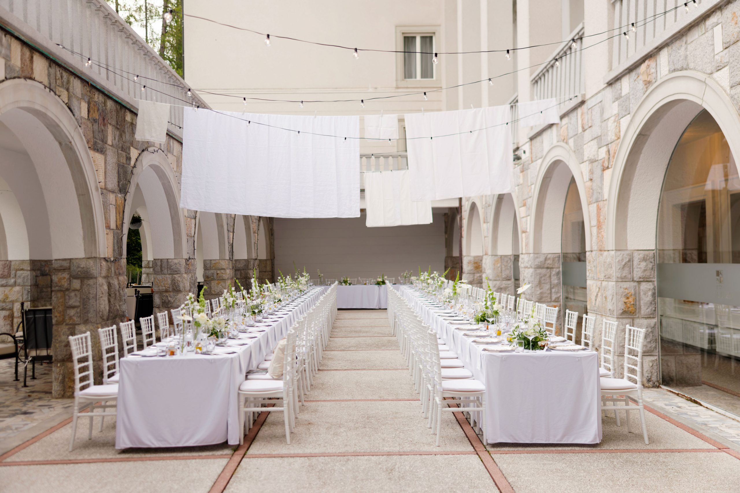 White sheets and string lights suspended above long wedding dining tables in the Vila Bled courtyard.