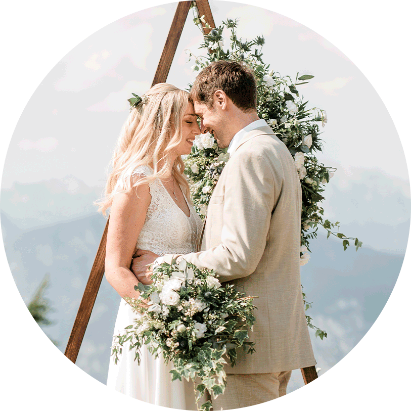 Young wedding couple from England enjoying romantic moments in front of wooden arch decorated with white and green flowers during their photo session at mountain Vogel.