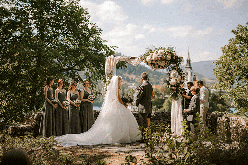 Bride and groom holding hands and their wedding party stand at wedding ceremony at vila Bled, Slovenia.