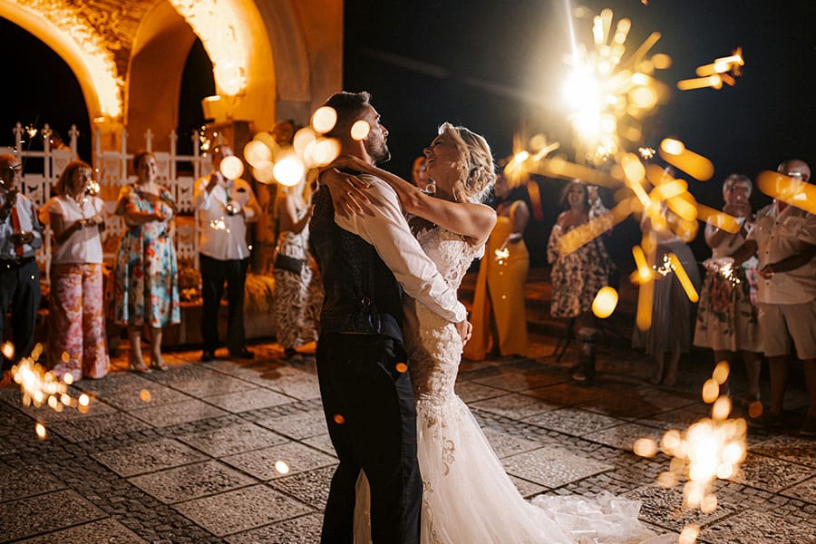 First dance of the Bride in stunning white wedding dress and Groom in a blue suit under stars and sparklers at Bled Castle terrace.