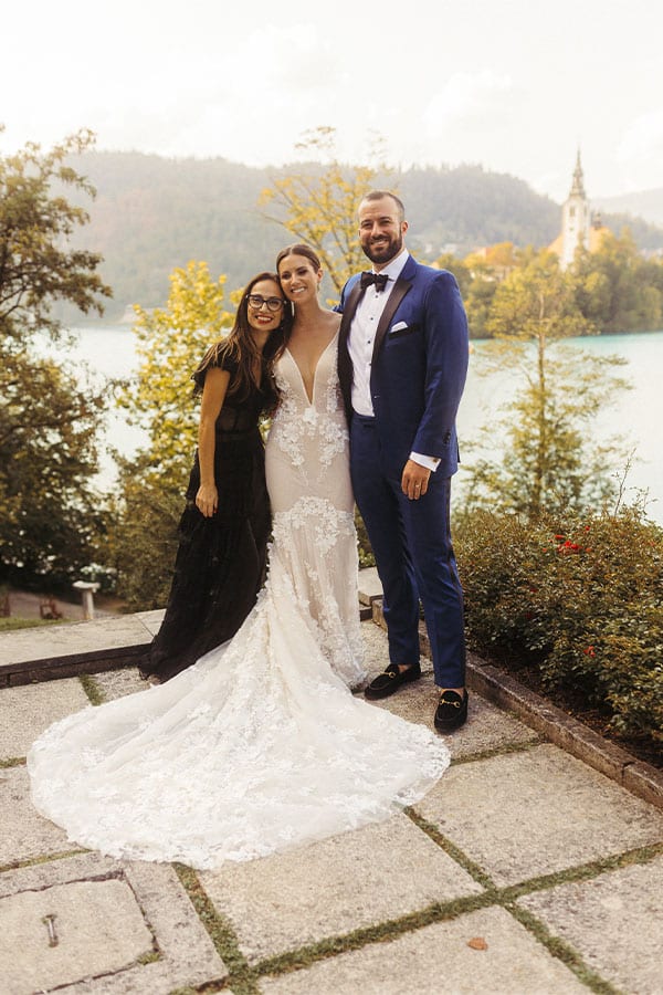 Bride in a stunning champagne lace wedding dress from Galia Lahav with her husband in a blue tux and their Bled wedding planner Petra Starbek at Villa Bled terrace.
