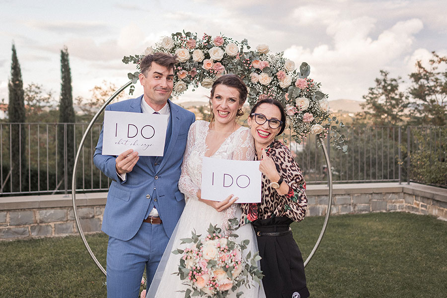 Newly married couples hold funny signs on a paper and with them is the lake Bled wedding planner Petra Starbek.